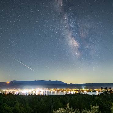 Una foto del cielo nocturno de Big Bear Lake, las estrellas brillan entre un meteoro que deja una estela junto a una galaxia.