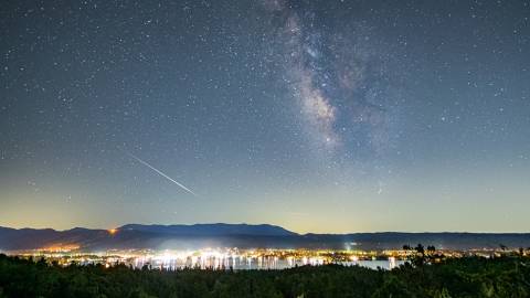 A photo of Big Bear Lake's night sky, the stars are shining brightly amongst a meteor leaving a trail next to a galaxy.