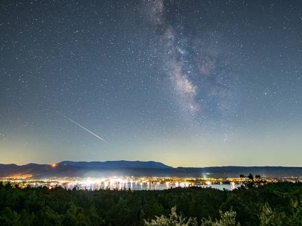 Una foto del cielo nocturno de Big Bear Lake, las estrellas brillan entre un meteoro que deja una estela junto a una galaxia.