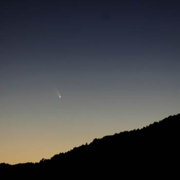 Foto de una montaña en silueta, la luna está en cuarto menguante mientras un cometa pasa a lo lejos.