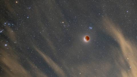 Un cielo nocturno oscuro y estrellado en Big Bear Lake: la luna, teñida de rojo, brilla visiblemente entre las estrellas luminosas.