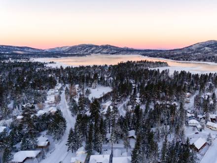 Una foto aérea de una nevada invernal en Big Bear Lake, el atardecer rosa anaranjado reflejándose en el lago.