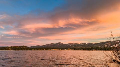 Una vista de la orilla del lago Big Bear: tanto el lago, ahí abajo, como las nubes, ahí arriba, resplandecen suavemente con los tonos rosa y naranja de la puesta de sol.