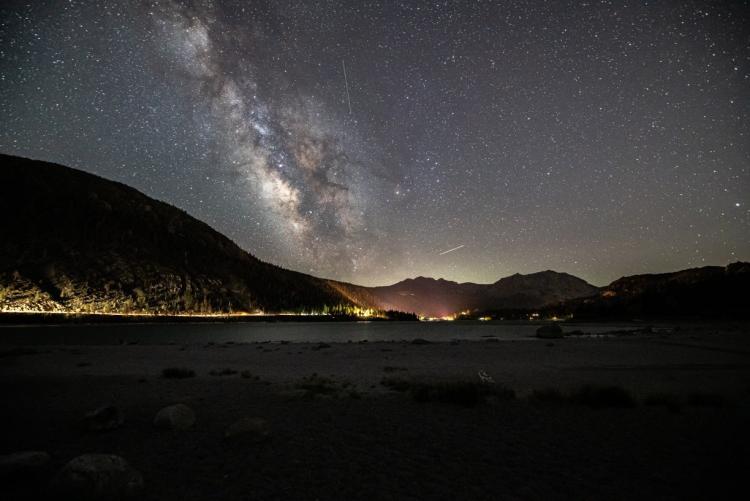 Una foto del cielo nocturno de Big Bear: la Vía Láctea y numerosas estrellas se divisan sobre las montañas, suavemente iluminadas.