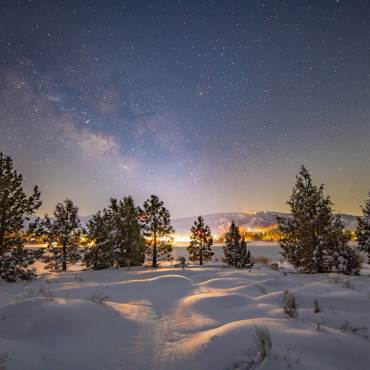 Una foto del cielo nocturno de Big Bear tomada durante el invierno después de una nevada, las estrellas brillantes y una galaxia son visibles.