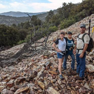 Una foto de voluntarios en una colina rocosa, uno de ellos lleva una mochila con palos largos como herramientas.