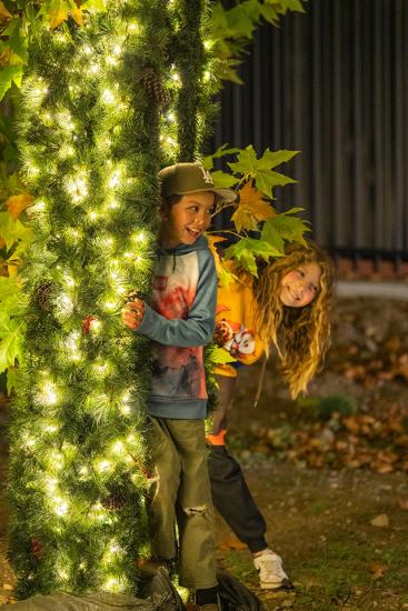Dos niños sonríen mientras se asoman desde detrás de una instalación luminosa en el evento «Wild Lights» del Big Bear Alpine Zoo.
