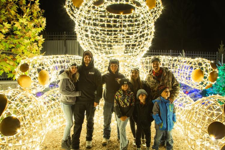 Una foto de una familia posando delante de una gran pantalla luminosa que parece un oso de peluche gigante.