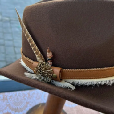 Un sombrero hecho a medida por Lucky Baldwin's: el sombrero, de cuero de color marrón, está adornado con una pluma que sobresale por un lado.