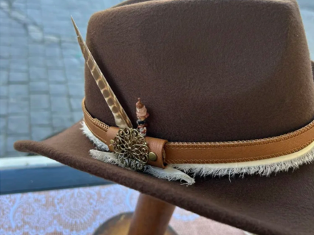 Un sombrero hecho a medida por Lucky Baldwin's: el sombrero, de cuero de color marrón, está adornado con una pluma que sobresale por un lado.