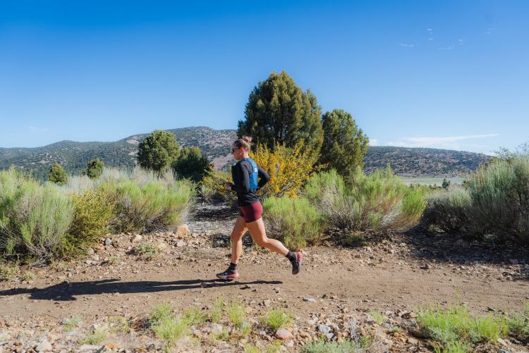 Una foto de una excursionista caminando por un sendero de tierra en Big Bear Lake, California; detrás de ella se ven las montañas y los árboles