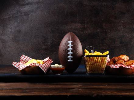 Un balón de fútbol sentado en una mesa de madera con aperitivos como patatas fritas y alitas de pollo. Imagen de archivo.