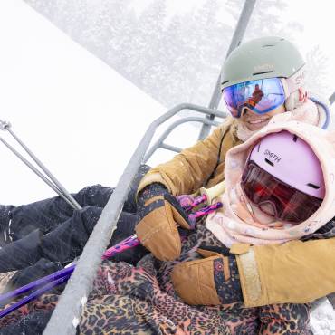 Una foto de dos personas con esquís en un telesilla en la estación de esquí Snow Summit, en Big Bear Lake, con nieve cayendo a su alrededor.
