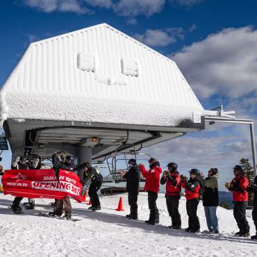 Una foto del día de apertura de la temporada de invierno 2025/26 de la estación de esquí Bear Mountain: alguien está cortando una pancarta mientras lleva puestos los esquís.
