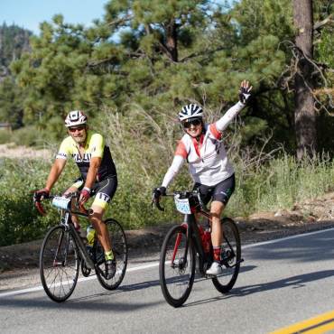 Dos ciclistas saludan durante su recorrido en bicicleta por el Tour de Big Bear en Big Bear Lake, CA