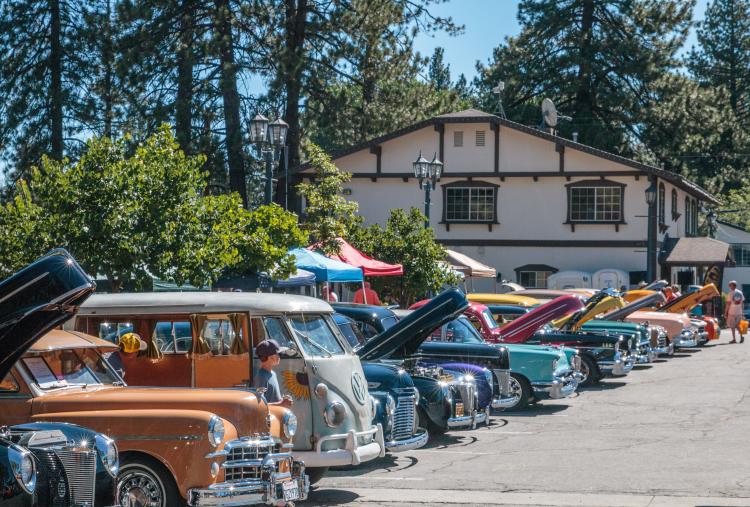 Coches antiguos brillantes y multicolores llenan un aparcamiento para la carrera Big Bear Lake Fun Run. Los capós se levantan para los espectadores.