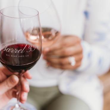 Una foto de las manos de dos personas sosteniendo una copa de vino con el logotipo de Barrel 33.