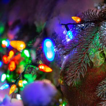 Una foto en primer plano de un árbol de Navidad decorado, está ligeramente cubierto de nieve y las luces brillan de varios colores.
