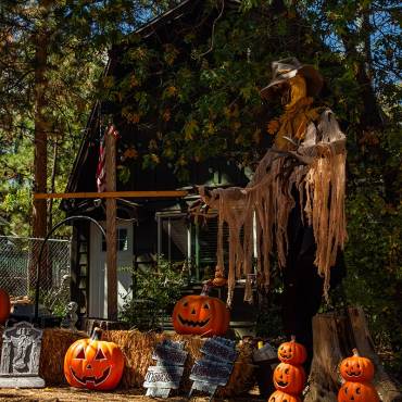 Una exposición del concurso «Espantapájaros y Día de los Muertos» de Big Bear de 2026: hay un espantapájaros gigante junto a unas tumbas y unas calabazas.