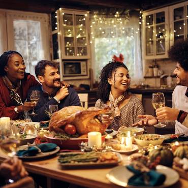 Un gran grupo de personas sentadas a una larga mesa con comida durante Acción de Gracias: sonríen y ríen.