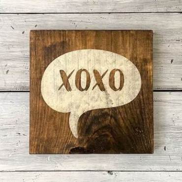Un cartel de madera pintado con XOXO sobre fondo blanco.