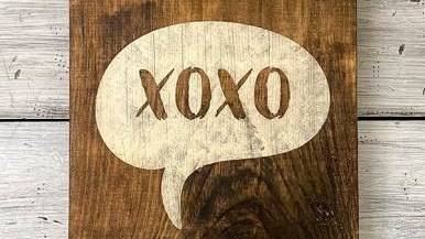 Un cartel de madera pintado con XOXO sobre fondo blanco.