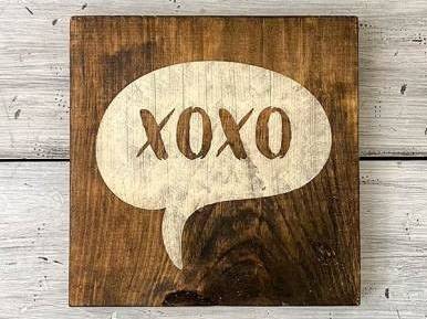 Un cartel de madera pintado con XOXO sobre fondo blanco.
