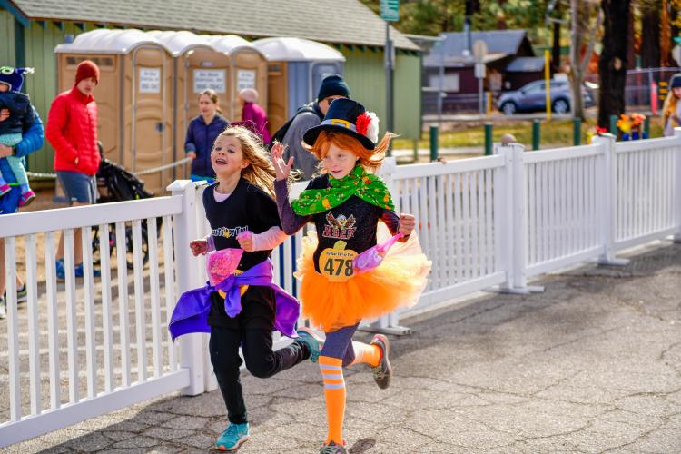 Una foto de dos chicas corriendo durante el Turkey Trot de Acción de Gracias, una de ellas disfrazada de duende.