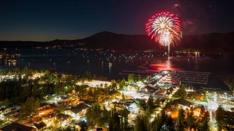 Unos fuegos artificiales rojos explotan sobre Big Bear Lake el 4 de julio. Las luces de los barcos y de la ciudad son visibles en esta escena nocturna.