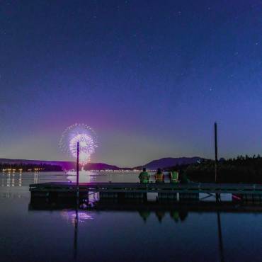 La gente se sienta en un muelle del lago Big Bear y admira el espectáculo pirotécnico del 4 de julio mientras los fuegos artificiales se reflejan en el lago.