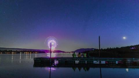 La gente se sienta en un muelle del lago Big Bear y admira el espectáculo pirotécnico del 4 de julio mientras los fuegos artificiales se reflejan en el lago.