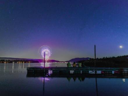 La gente se sienta en un muelle del lago Big Bear y admira el espectáculo pirotécnico del 4 de julio mientras los fuegos artificiales se reflejan en el lago.