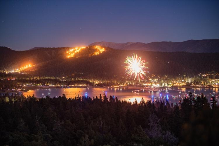Brillantes fuegos artificiales iluminan el cielo durante la celebración del 4 de julio en Big Bear Lake; se divisan las montañas y el lago.