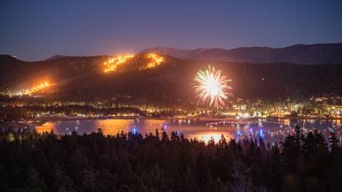 Brillantes fuegos artificiales iluminan el cielo durante la celebración del 4 de julio en Big Bear Lake; se divisan las montañas y el lago.