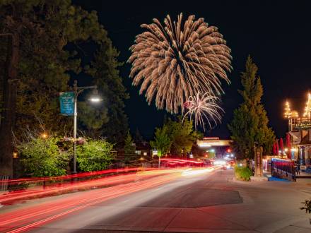 Una larga exposición de luces de cola rojas en The Village en Big Bear Lake. Fuegos artificiales del 4 de julio son visibles en el cielo nocturno.