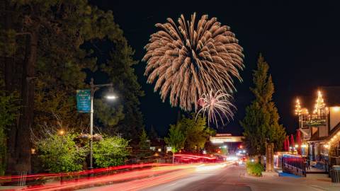 Una larga exposición de luces de cola rojas en The Village en Big Bear Lake. Fuegos artificiales del 4 de julio son visibles en el cielo nocturno.