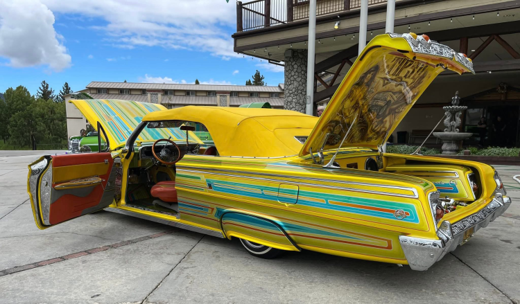 Una foto de un lowrider aparcado frente al Holiday Inn. El coche es amarillo con rayas azul claro y capota.