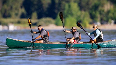 Un grupo de tres en un kayak durante LakeFest, trabajando juntos para remar con sus remos, salpicando agua hacia arriba a medida que avanzan.
