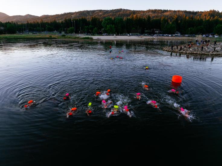 Una imagen tomada con dron durante el LakeFest de los nadadores participantes, con el agua reflejando suavemente las montañas del fondo.