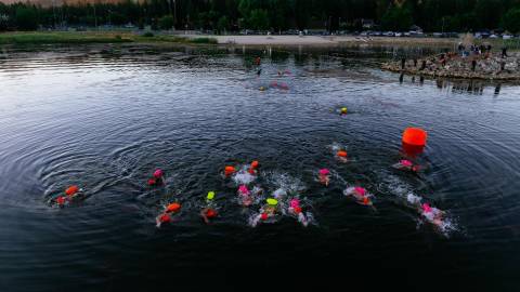 Una imagen tomada con dron durante el LakeFest de los nadadores participantes, con el agua reflejando suavemente las montañas del fondo.