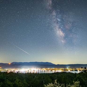 Una amplia vista panorámica del lago Big Bear por la noche: se divisan la Vía Láctea y las estrellas sobre la localidad y el lago a sus pies.