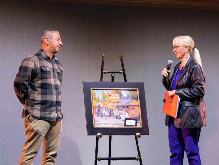 Una foto de la ceremonia de entrega de premios Plein Air, en la que se ve a Diane Moore hablando con el ganador del tercer puesto del concurso.