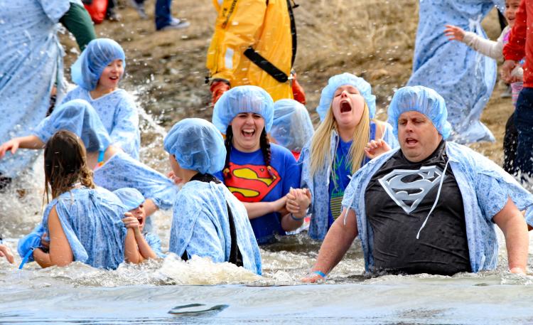 Un grupo de hombres y mujeres llevan batas y gorros de hospital mientras se zambullen en el lago Big Bear durante la zambullida polar de Big Bear.