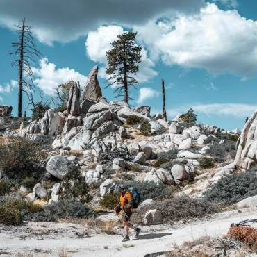 una persona caminando entre formaciones rocosas en un día soleado durante el evento de senderismo Highlander Adventure en Big Bear