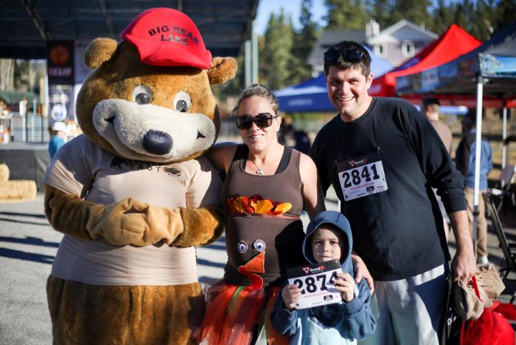 Una madre, un padre y un niño sonríen para una foto con la mascota del Big Bear Turkey Trot durante el Big Bear Turkey Trot.