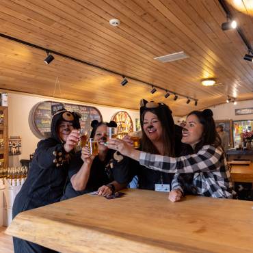 Cuatro mujeres están de pie en una mesa brindando con cerveza mientras visten sus disfraces de oso para el Big Bear Lake Bear Crawl.