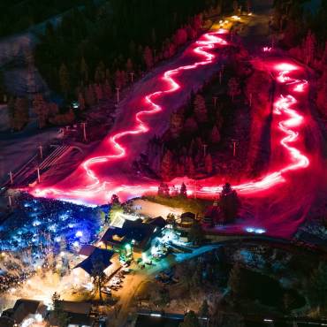 Una vista aérea de Snow Summit durante el desfile de antorchas de Nochevieja: se ven estelas de luz roja a lo largo de la montaña.