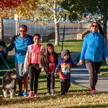 Una familia de cinco miembros con tres niños pequeños y un perro paseando por el parque entre las hojas caídas durante el otoño.