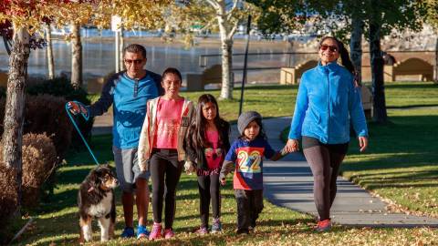 A family of five with three small children and a dog walking at the park walking through fallen leaves during Autumn.