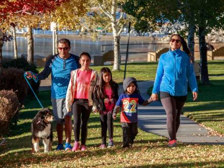 Una familia de cinco miembros con tres niños pequeños y un perro paseando por el parque entre las hojas caídas durante el otoño.